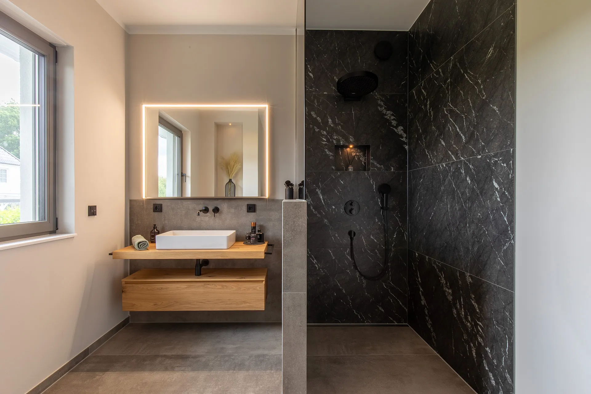 Header eines Stonehenge-Badezimmers mit Naturstein-Dusche und Waschtisch aus Holz vom Handwerksunternehmen Prehn & von Hoeßlin GmbH & Co. KG.