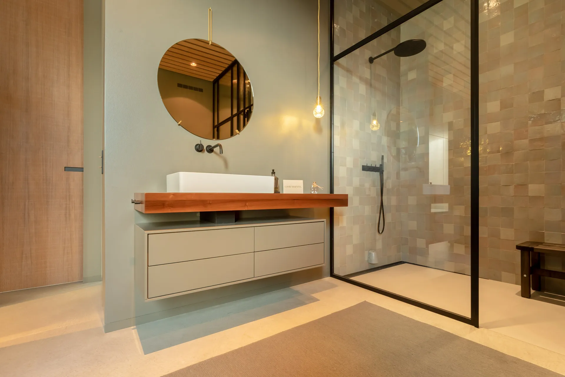 Waschtisch mit Holz und rundem Spiegel im Penthouse-Referenzbad vom Handwerksunternehmen Prehn & von Hoeßlin GmbH & Co. KG.