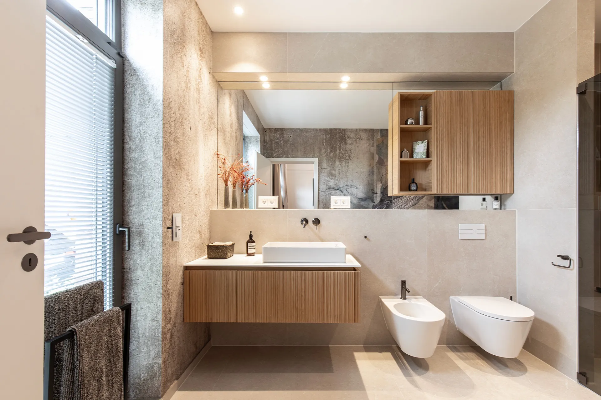 Gesamtübersicht eines Referenzbads mit schwebendem Waschtisch aus Holz mit großem Spiegel, WC und Bidet vom Handwerksunternehmen Prehn & von Hoeßlin GmbH & Co. KG.