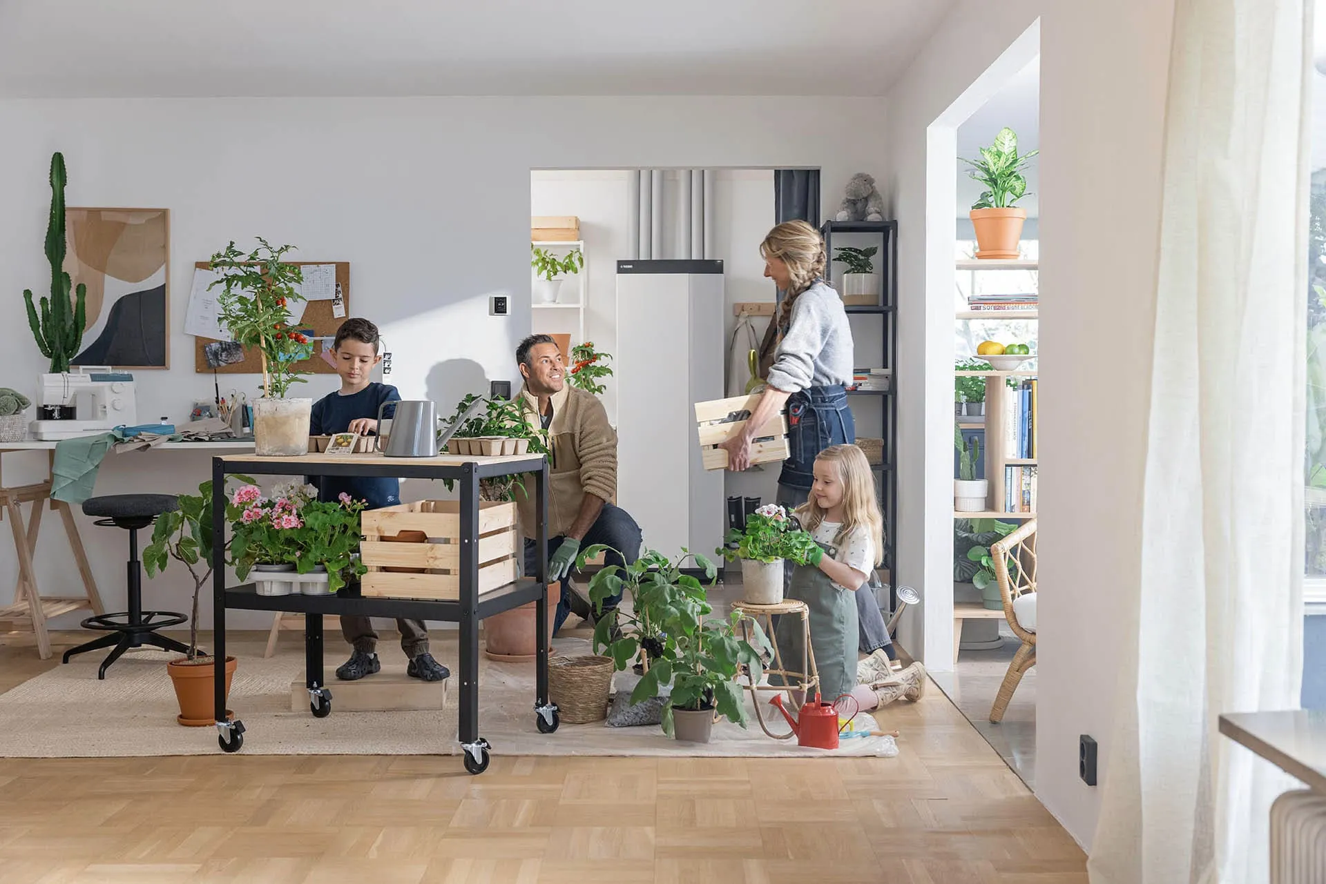 Eine vierköpfige Familie arbeitet gemeinsam in einem hellen Wohnzimmer an der Pflege von Zimmerpflanzen. Im Hintergrund steht eine moderne Wärmepumpen-Inneneinheit neben offenen Regalen und Pflanzenarrangements.