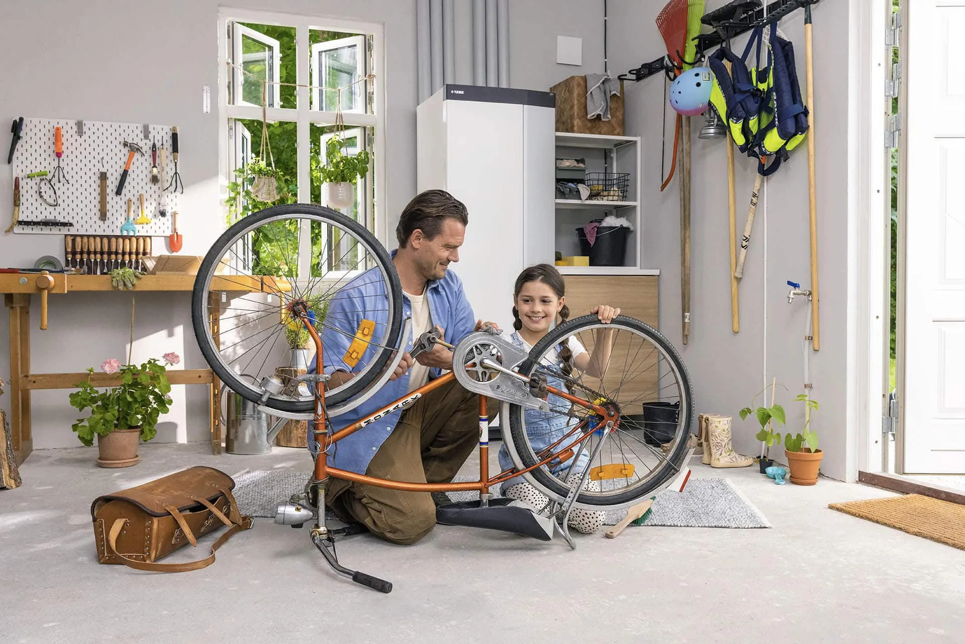 Ein Vater und seine Tochter reparieren gemeinsam ein Fahrrad in einer aufgeräumten Garage.