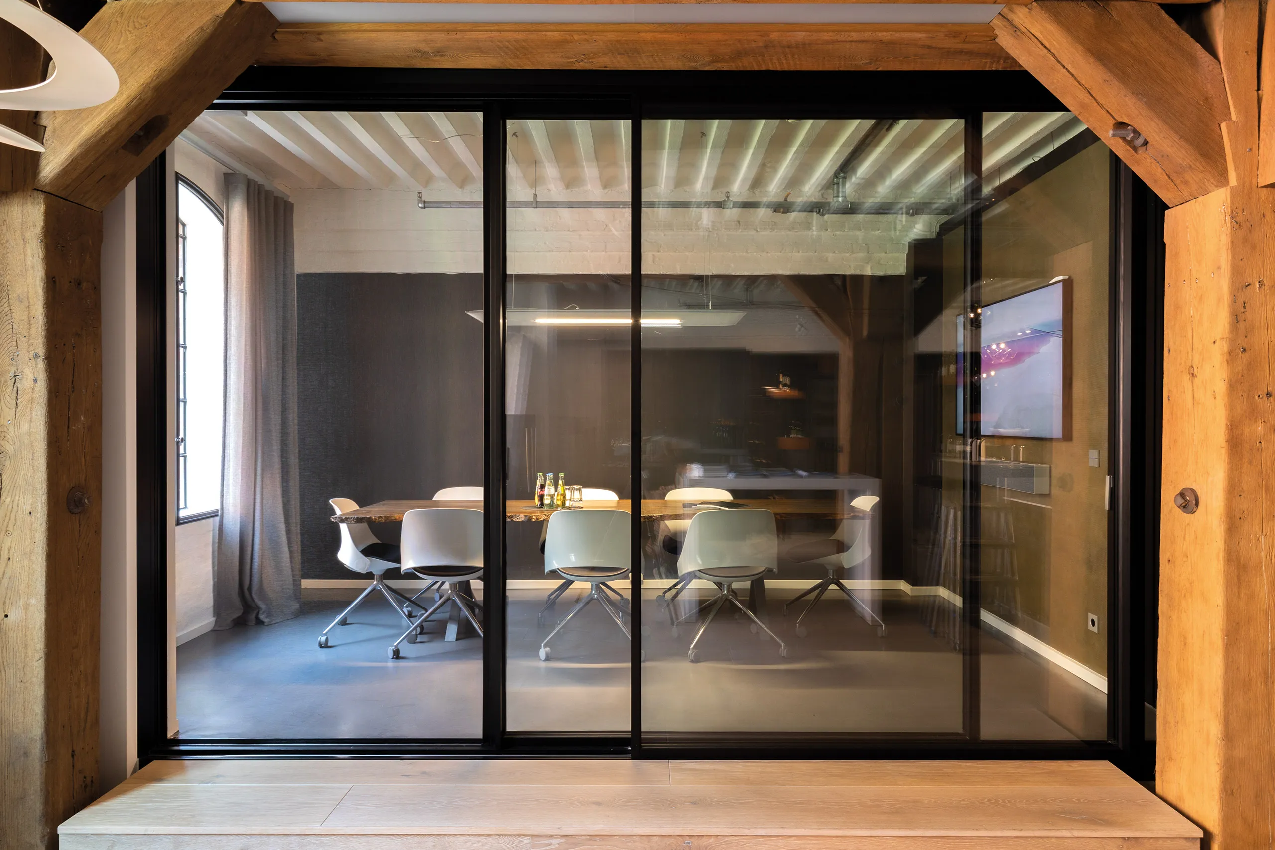 Besprechungsraum mit großem Holztisch, weißen Stühlen und Glas-Schiebetüren in schwarzem Metallrahmen in der Badausstellung der Prehn & von Hoeßlin GmbH & Co. KG in Hamburg.