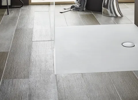 Nahaufnahme einer flachen Acryl-Duschwanne, eingebettet in ein Badezimmer mit grauen, holzstrukturierten Fliesen. Minimalistisches und modernes Design.