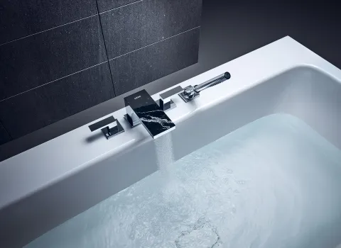 Eine moderne Badewanne mit einer stilvollen, rechteckigen Armatur aus glänzendem Metall und einer schwarzen Marmoroberfläche.