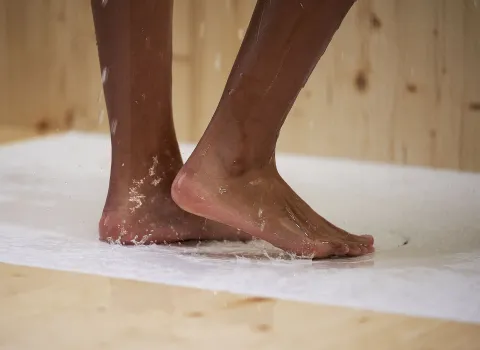 Die Füße einer Person berühren eine weiße, leicht nasse Oberfläche, auf der sich Wassertropfen sammeln.