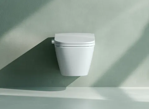 Ein modernes Dusch-WC ist wandhängend an einer hellgrünen Badezimmerwand montiert und wirft einen langen Schatten.