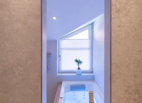 Sicht im Spiegel auf die beleuchtete Badewanne und Dachschräge im Referenzbad von Prehn & von Hoeßlin GmbH & Co. KG.