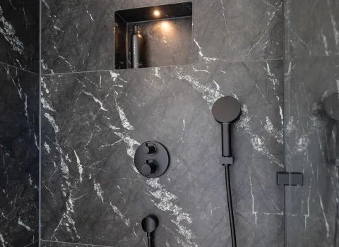 Dusche mit schwarzer Armatur und Wand in Marmoroptik im Referenzbad der Prehn & von Hoeßlin GmbH & Co. KG.