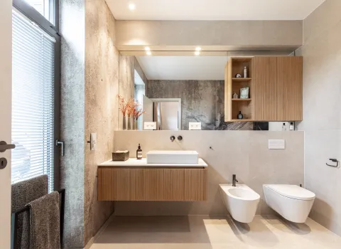 Gesamtübersicht eines Referenzbads mit schwebendem Waschtisch aus Holz mit großem Spiegel, WC und Bidet vom Handwerksunternehmen Prehn & von Hoeßlin GmbH & Co. KG.