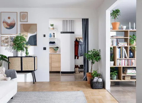 Ein modern eingerichtetes Wohnzimmer mit Blick auf einen Flur, in dem eine schlanke Wärmepumpe installiert ist