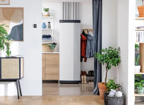 In einem hellen, modern eingerichteten Flur steht eine kompakte Wärmepumpe dezent zwischen Holzregalen und einer offenen Garderobe.
