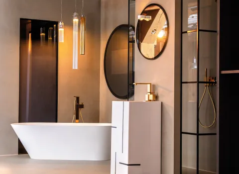 Design-Bad mit freistehender weißer Badewanne, goldenen Armaturen, runden Spiegeln und moderner Akzentbeleuchtung in der Badausstellung der Prehn & von Hoeßlin GmbH & Co. KG in Hamburg.