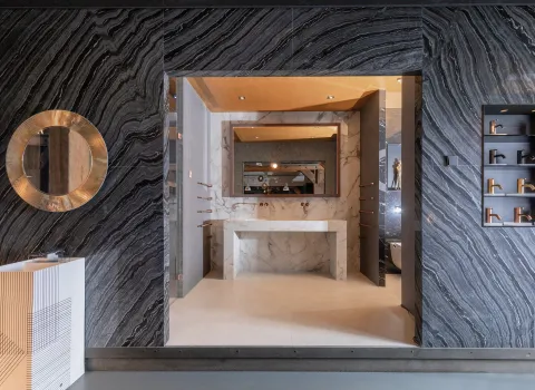 Ausstellungsbereich mit markanter Natursteinwand, rundem Spiegel, modernem Waschtisch aus weißem Marmor und Armaturen-Präsentation in der Badausstellung der Prehn & von Hoeßlin GmbH & Co. KG in Hamburg.