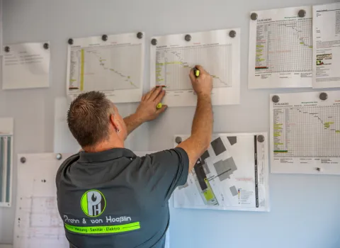Mitarbeiter von Prehn & von Hoeßlin markiert Bauablaufpläne an einer Wand, während er einen Textmarker benutzt.