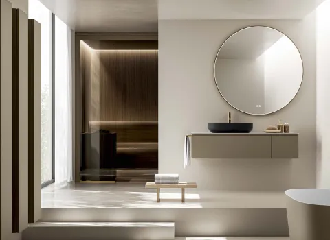Modernes Badezimmer von Stocco mit schwebendem Waschtisch, rundem Spiegel, Aufsatzbecken und integrierter Sauna im Hintergrund.