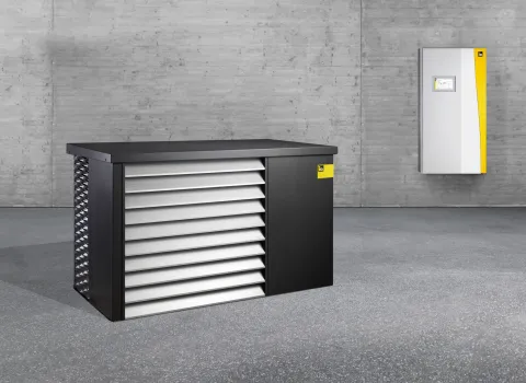 Innen- und Außeneinheit der Wärmepumpe iDM AERO ALM 2-8 und 4-12 in einem leeren, grauen Raum.