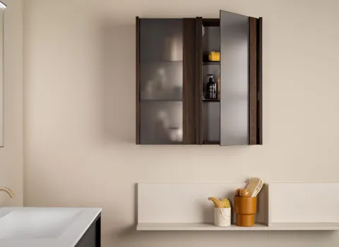 Badezimmerdetail von Stocco mit geöffneter Spiegelschranktür in dunkler Holzoptik, Wandablage und goldener Armatur.