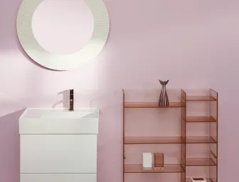 Ein kleines, modernes Badezimmer mit hellrosa Wänden zeigt einen weißen Waschtisch mit eckigem Design und einem runden, geriffelten Spiegel darüber.