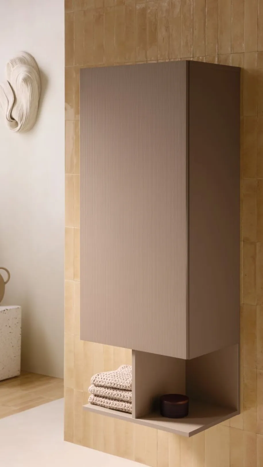 Ein ockerfarbener Hängeschrank der Serie Balcoon von Duravit ist an einer goldbraun gefliesten Wand angebracht.