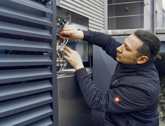 Ein Techniker überprüft eine Elektroinstallation an einer Außeneinheit, während er sorgfältig Kabel in einem offenen Schaltkasten anschließt.